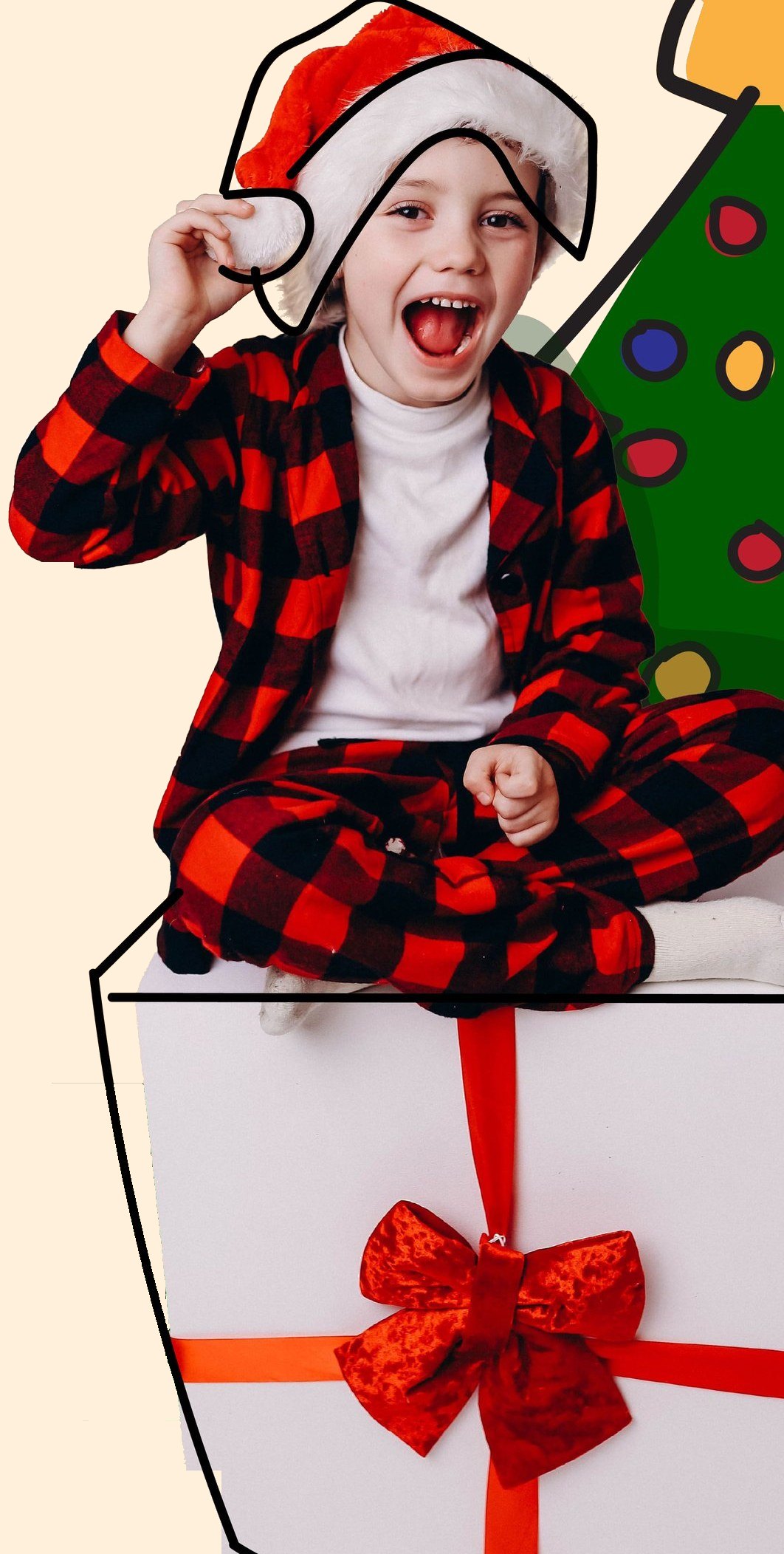 A smiling boy in a Santa hat and plaid pajamas sits on a wrapped gift beside a Christmas tree